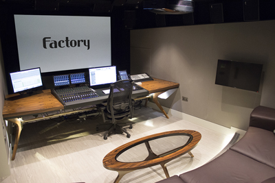 A professional music studio featuring a large mixing console, multiple monitors, and a wooden desk.