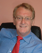 A man with blond hair and glasses wearing a blue dress shirt and a red patterned tie.