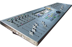 A large, silver digital audio mixing console with numerous faders, knobs, and buttons.