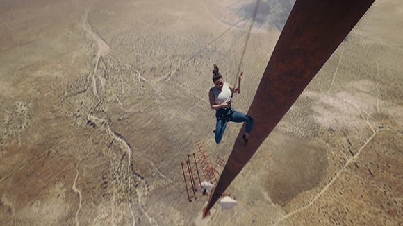 A person in athletic wear climbs a long, rusted metal beam suspended high above a vast desert terrain.
