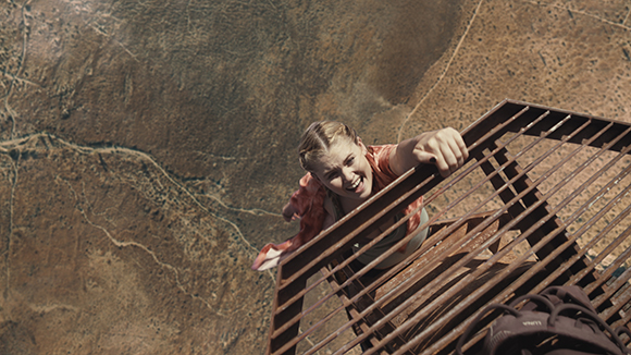 A woman climbs a metal ladder structure high above a vast, arid landscape.