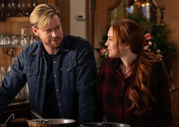 A blonde man in a denim shirt and a red-haired woman in a plaid shirt look at each other.