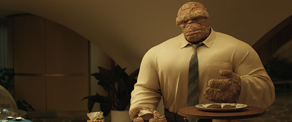 A large, orange, rocky-skinned humanoid in a tan shirt and tie holds a small plate of food.