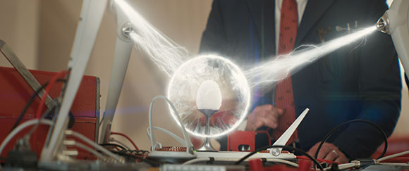 Electrical arcs discharge from two metal terminals toward a glowing central sphere in a laboratory setting.