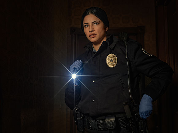 A police officer in uniform holds a bright flashlight in a dark, dimly lit room.
