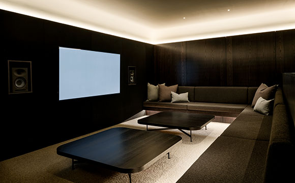 A dark home theater room with wood-paneled walls, a large screen, and low seating.
