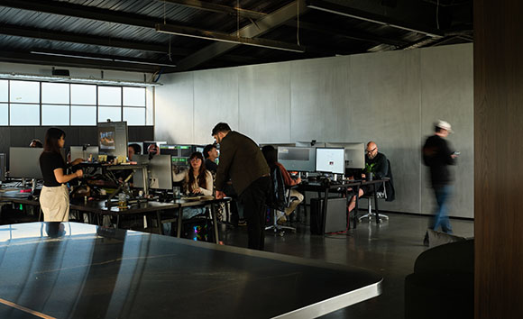 People working at computer desks in a large, industrial-style open office space.