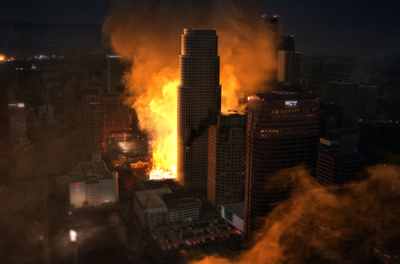 Massive orange flames and thick smoke billowing between city skyscrapers at night.