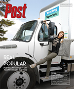 A woman in a t-shirt and pants poses with one leg extended next to the driver's side door of a white moving truck. She holds