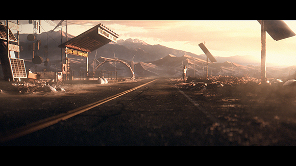 A wide shot of a dusty desert road leading toward mountains under a hazy, golden sky.