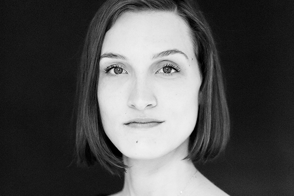 Black and white headshot of a woman with short dark hair looking directly forward against a dark background.