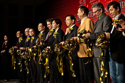 A line of men in suits holding large gold ceremonial scissors to cut a gold ribbon.