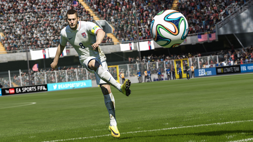 A soccer player in a white uniform kicks a colorful soccer ball on a green field in a crowded stadium.