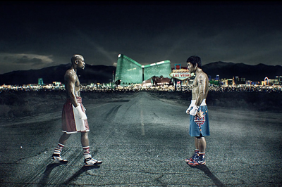 Two shirtless boxers in trunks face each other on a dark road with Las Vegas lights in the distance.