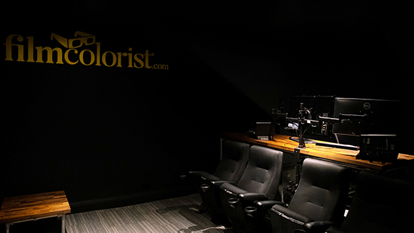 A dark studio featuring a row of black chairs facing a desk with multiple computer monitors.