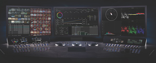 Three large monitors displaying video editing software and color grading tools above a control console.