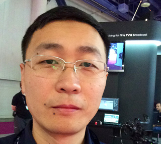 Close-up portrait of an East Asian man wearing rimless glasses in a professional setting.