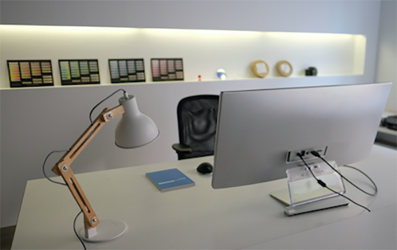 A white desk featuring a computer monitor, a wooden desk lamp, and a blue notebook in a bright office.
