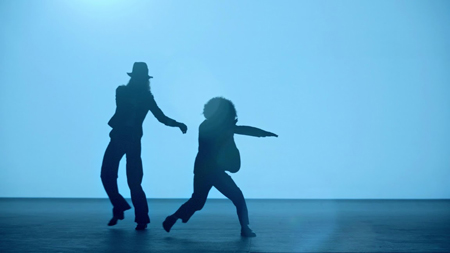 Silhouettes of two people dancing against a bright blue background.