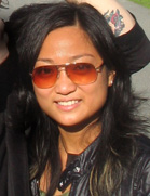 A smiling woman with long dark hair and orange-tinted aviator sunglasses.