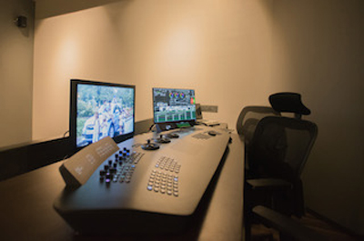 A video production console with two monitors and a black office chair in a dimly lit room.