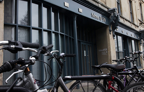 Several bicycles parked in the foreground in front of a dark blue storefront labeled films@59.
