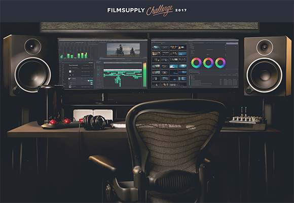 A dark video editing suite featuring dual monitors displaying editing software, large studio speakers, and a desk with audio
