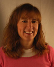 A woman with shoulder-length reddish-brown hair and bangs smiling in a pink shirt.