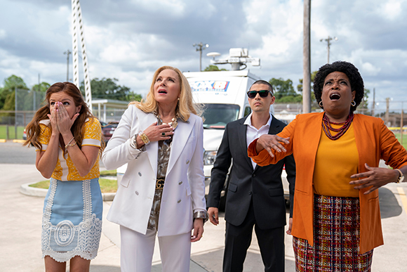 Four people stand outdoors looking up at the sky with expressions of shock and fear.