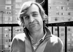 Black and white portrait of a man with medium-length hair wearing a collared shirt and sweater.