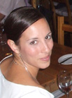 A woman with dark hair pulled back, wearing a white top and silver necklace.