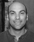 Black and white headshot of a bald man with dark eyebrows smiling at the camera.
