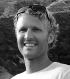 A smiling man with curly hair and sunglasses resting on top of his head.