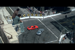 A red sports car and a silver sedan drive through a street intersection marked with circular tire tracks.