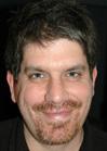 A man with dark, messy hair and a goatee smiling.
