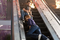 A man and woman fall down an escalator as flames erupt nearby.