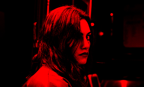 A woman with dark hair looks over her shoulder under intense red lighting.