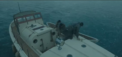 People in dark clothing working on the deck of a small white motorboat in the ocean.
