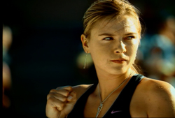 A blonde woman in athletic wear looks forward with a determined expression and a clenched fist.