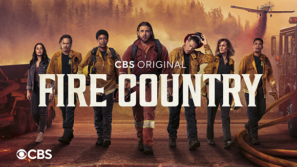Seven firefighters walk toward the camera against a smoky forest background with a plane flying overhead.