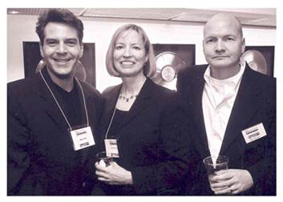 Three people in formal attire standing together at an event, wearing name tags.