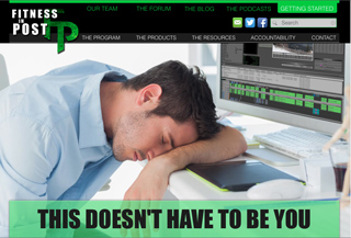 A man in a light blue shirt sleeps with his head on his arms at a desk next to a computer.