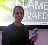 A man in a dark blazer smiling and holding a small trophy in front of a Flame Award sign.