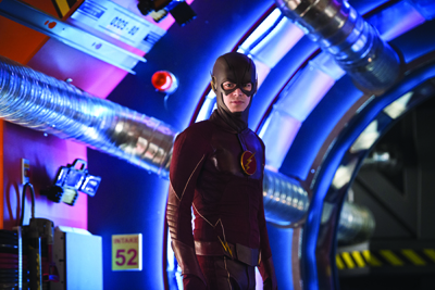 A person in a red superhero suit with a lightning bolt emblem stands in a blue and purple lit tunnel.