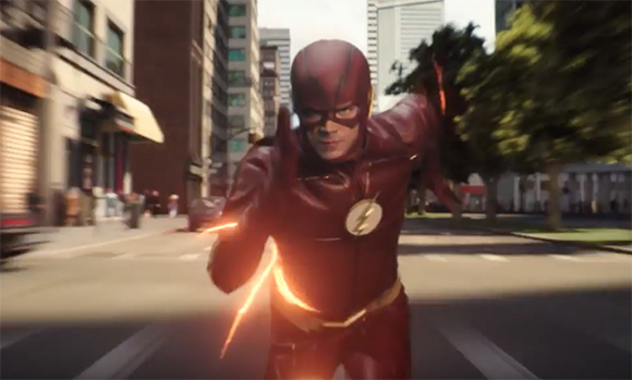 A person in a red superhero suit with lightning accents runs toward the camera on a city street.