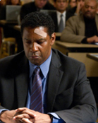 A man in a dark suit and blue tie sits with hands clasped, a bandage on his forehead.