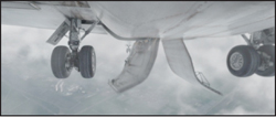 The underside of an airplane showing deployed landing gear and flaps against a cloudy sky.