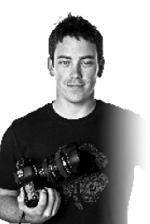 Black and white portrait of a man wearing a dark t-shirt and holding a professional camera.