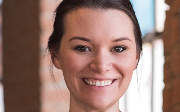 A close-up portrait of a smiling woman with dark hair pulled back.