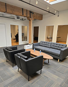 Gray sofas and armchairs arranged around a wooden coffee table in a modern office lounge.